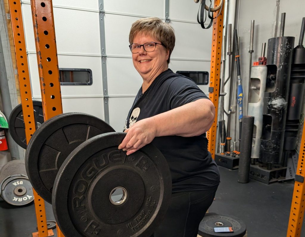 Person smiling while holding weight plates in a gym setting.